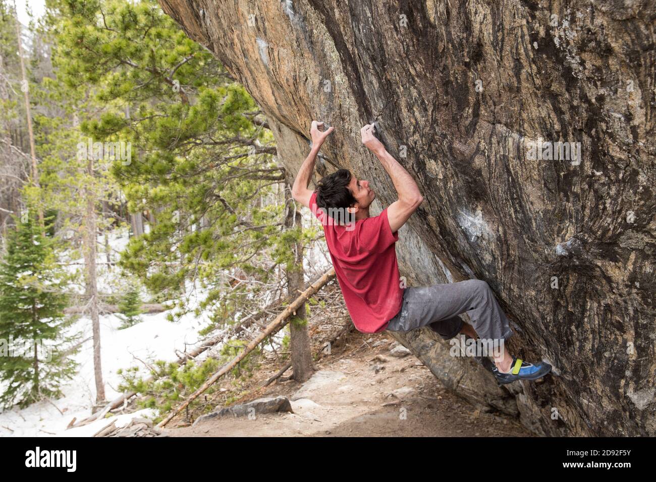 Athletic male climbs outside on a boulder in the alpine forest Stock Photo