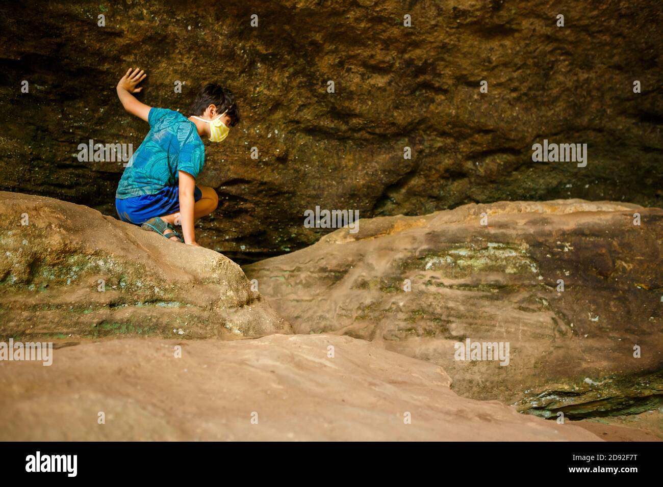 A boy crawls across boulders against rock wall in sandstone gorge Stock Photo