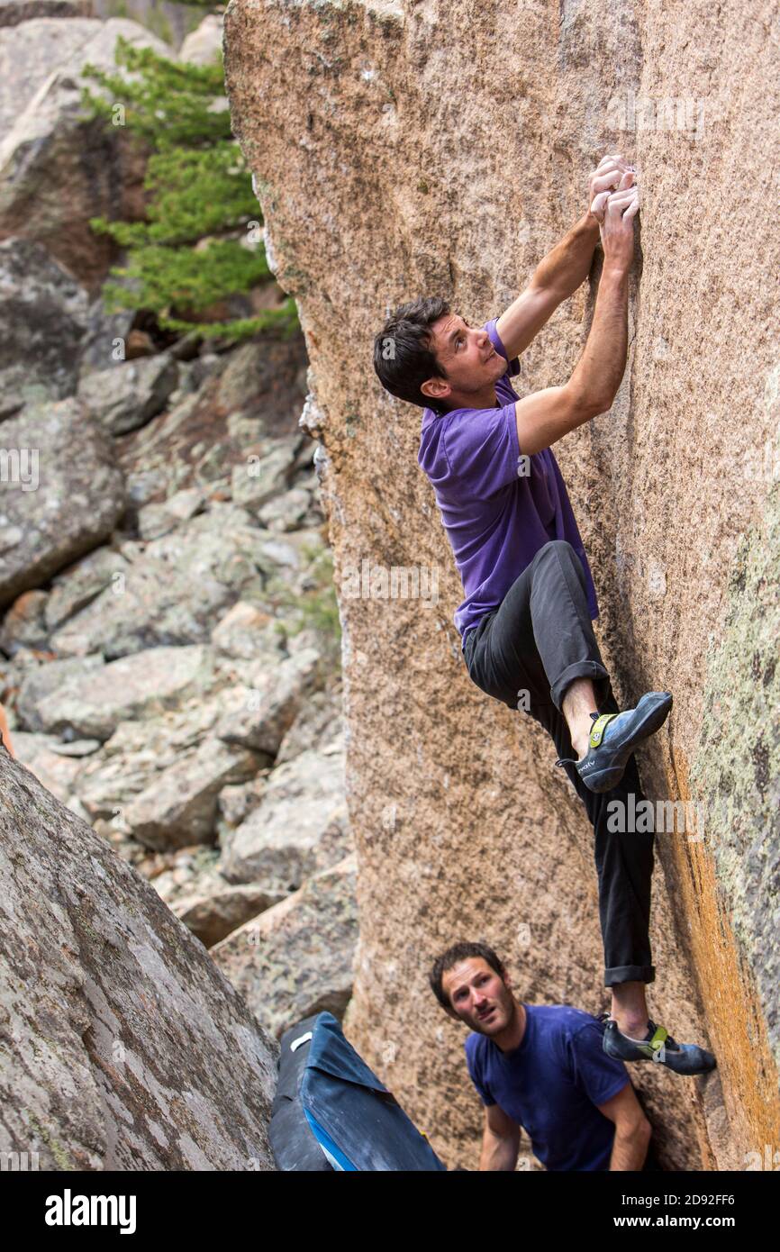 Athletic male climbs outside on a boulder with male spotter Stock Photo