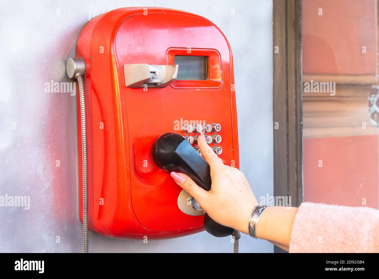a woman's hand dials a phone number on a public pay phone Stock Photo