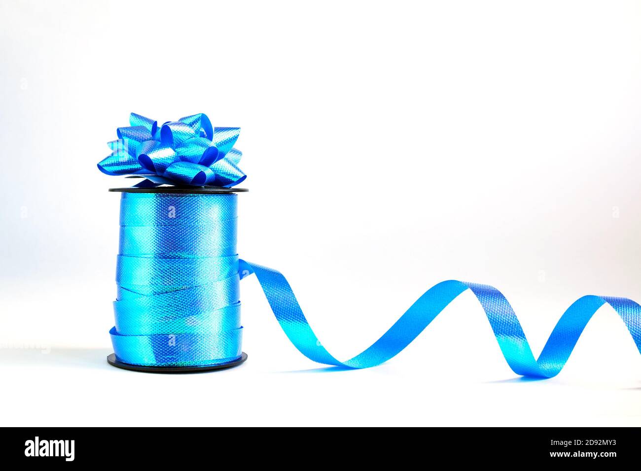 Spool of blue wavy ribbon and decorative gift bow on white background Stock Photo