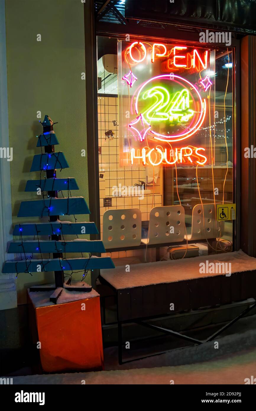 Open 24 hours neon sign on cafe, wooden Christmas tree with garlands at night in winter Stock Photo