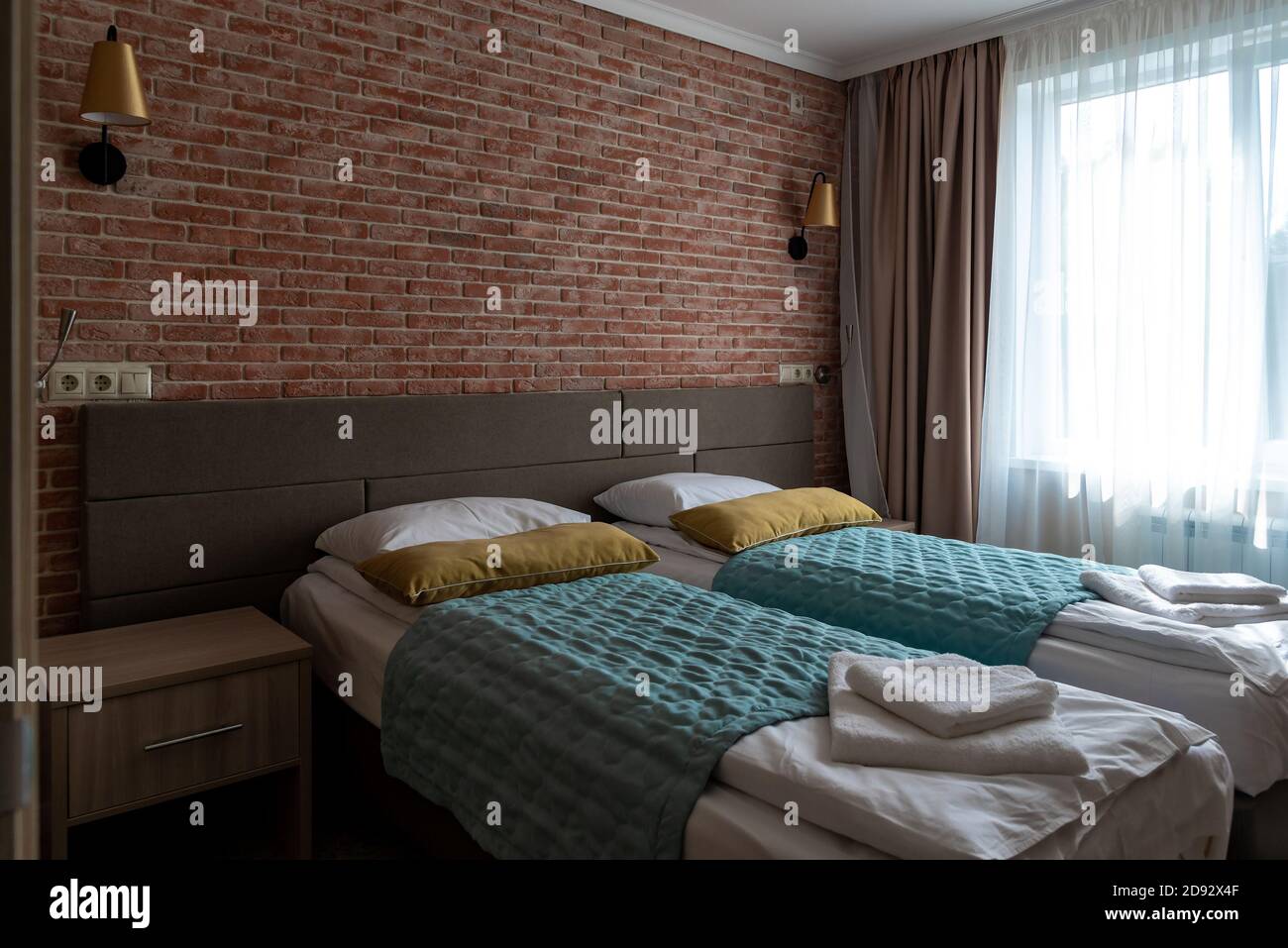 Empty hotel room with beds near red brick wall and window Stock Photo