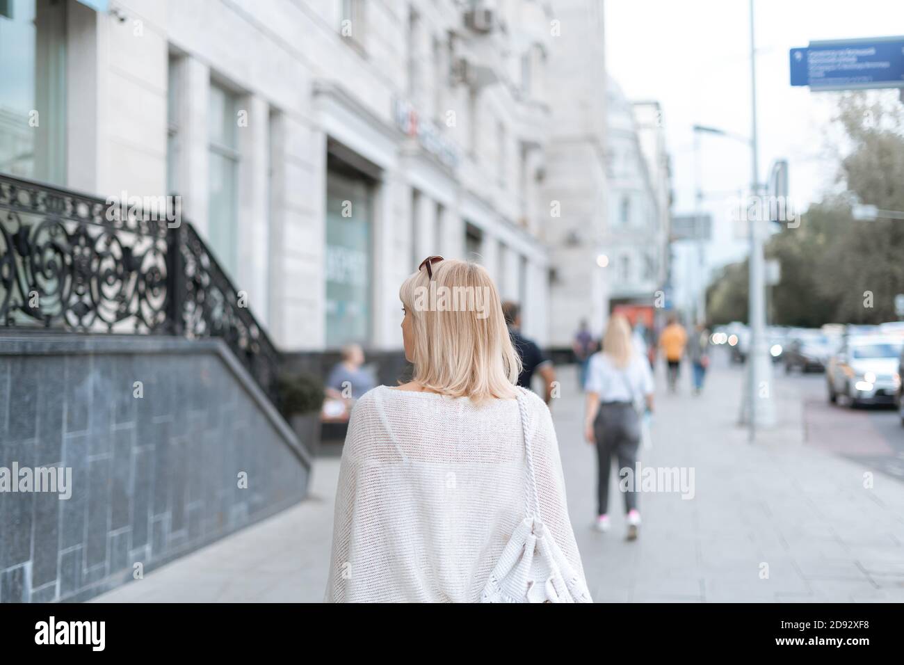 Back view of blonde adult woman with backpack walking on city street ...