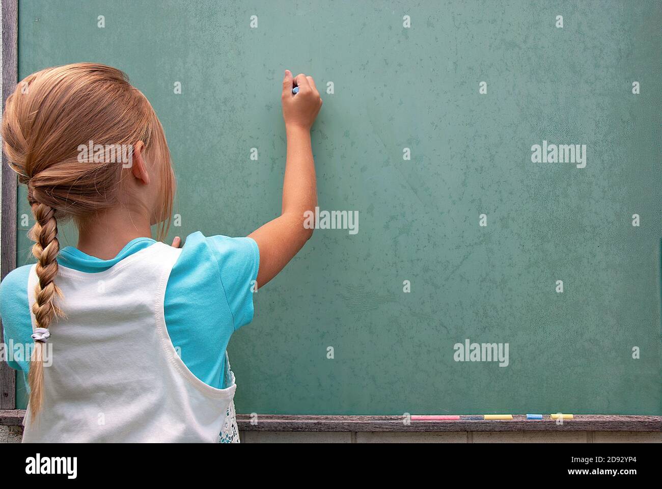 young Caucasian girl writing with chalk on green chalkboard Stock Photo