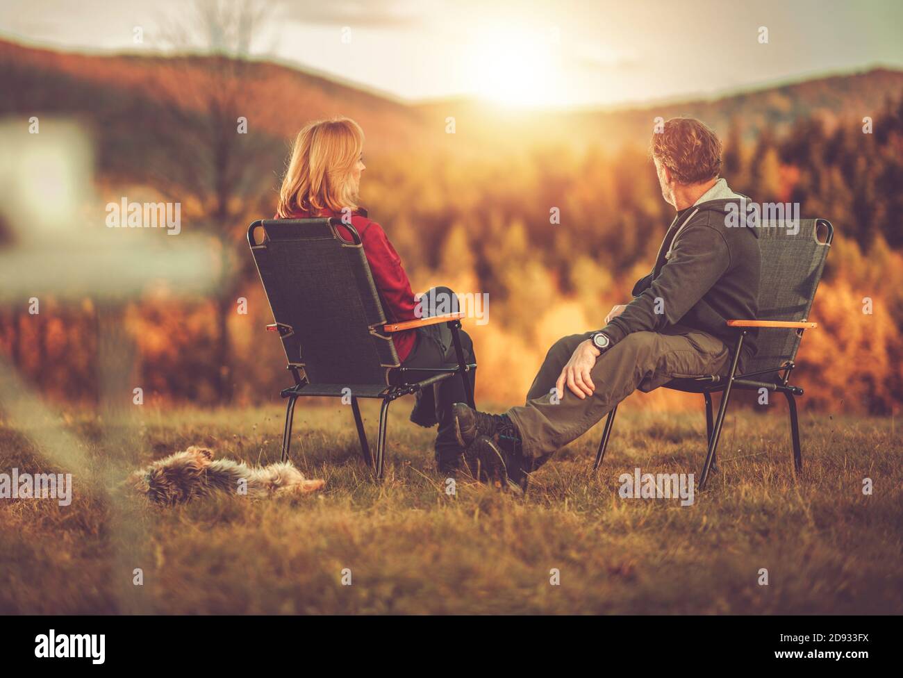 Caucasian Couple in Their 40s Seating in Front of Scenic Vista Enjoying Their Life and the Nature. Australian Silky Terrier Next to Chairs. Colorful F Stock Photo