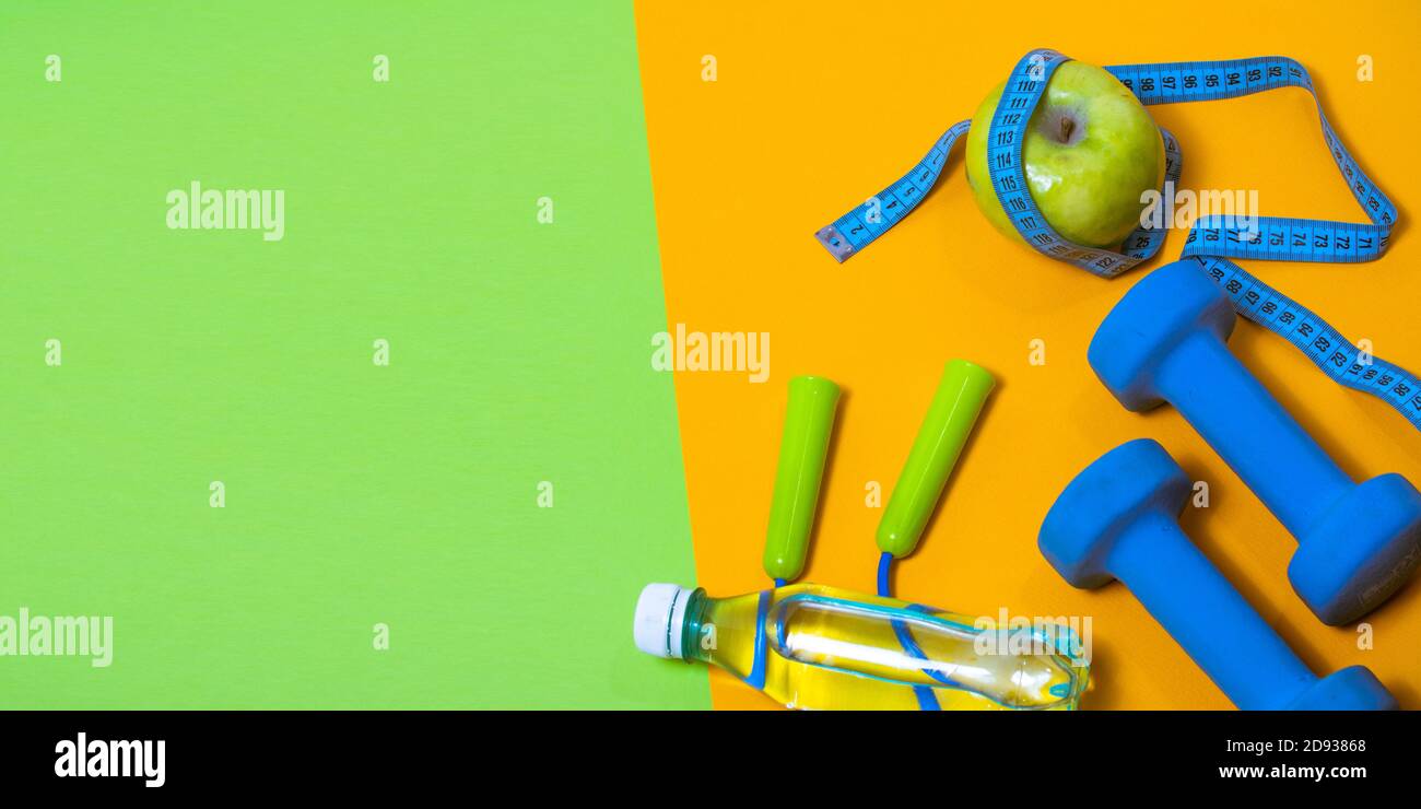 Fitness concept banner with dumbbells, jump ropes and measuring tape on a green and yellow background. Stock Photo