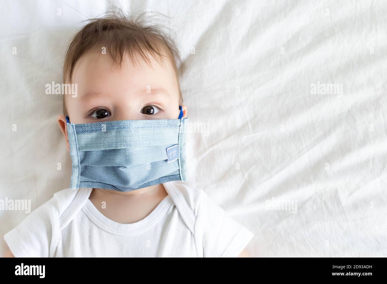 Little baby in medical mask on white bedding sheet. Concept covid19