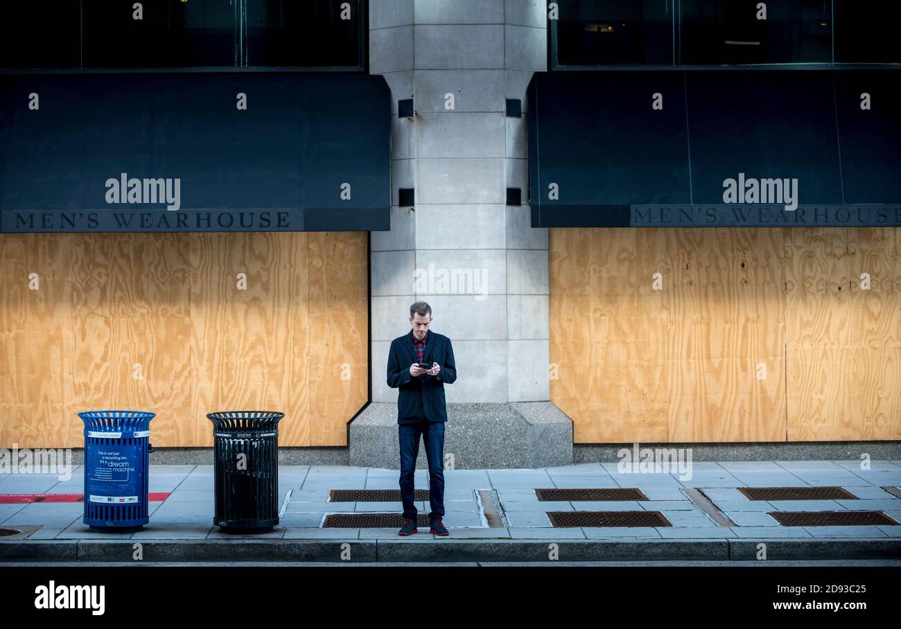 Washington DC, USA, Nov 2nd, 2020, A man looking at his phone while in front of a boarded up storefront. Washington DC is being boarded up in preparation of possible election 2020 related riots on Nov 3rd in  Washington DC, USA, Credit: Yuriy Zahvoyskyy/ Alamy Live News Stock Photo