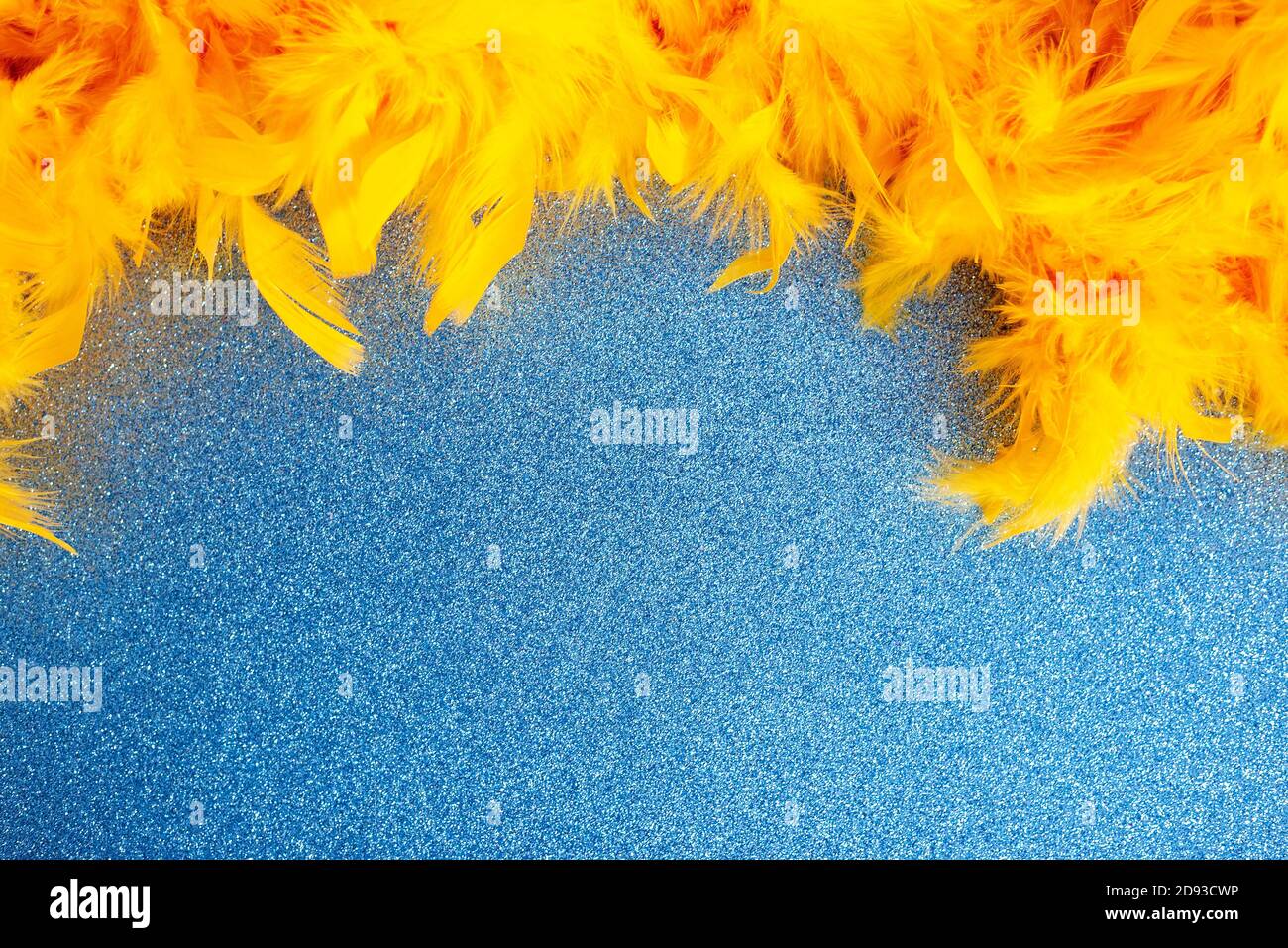 Yellow feather boa lying on light blue sparkling background Stock Photo