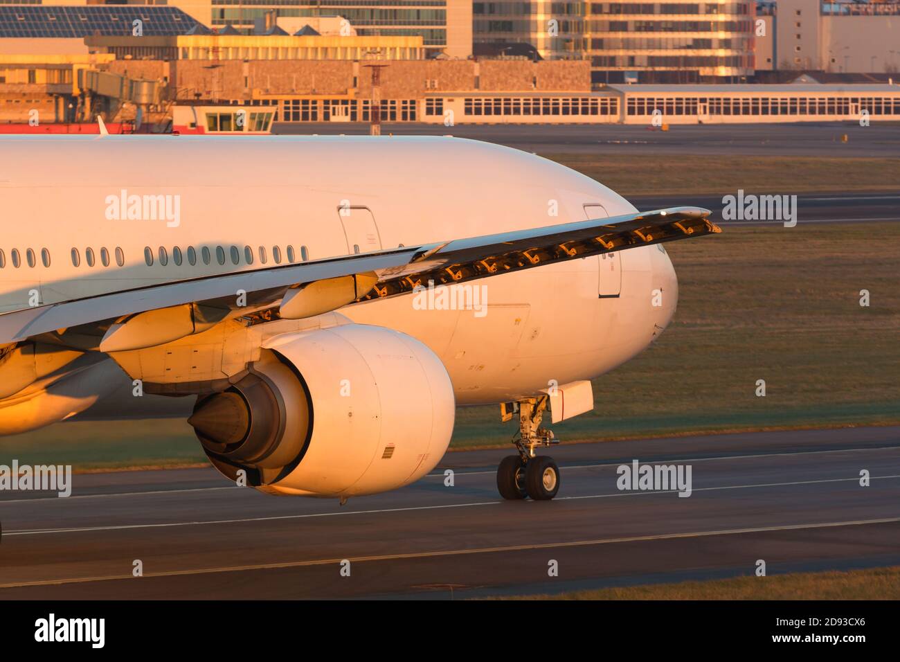 Close up of wide-body passenger aircraft with wing and engine taxing on the runway during sunset. Airplane turns on runway. Transportation, aviation. Stock Photo