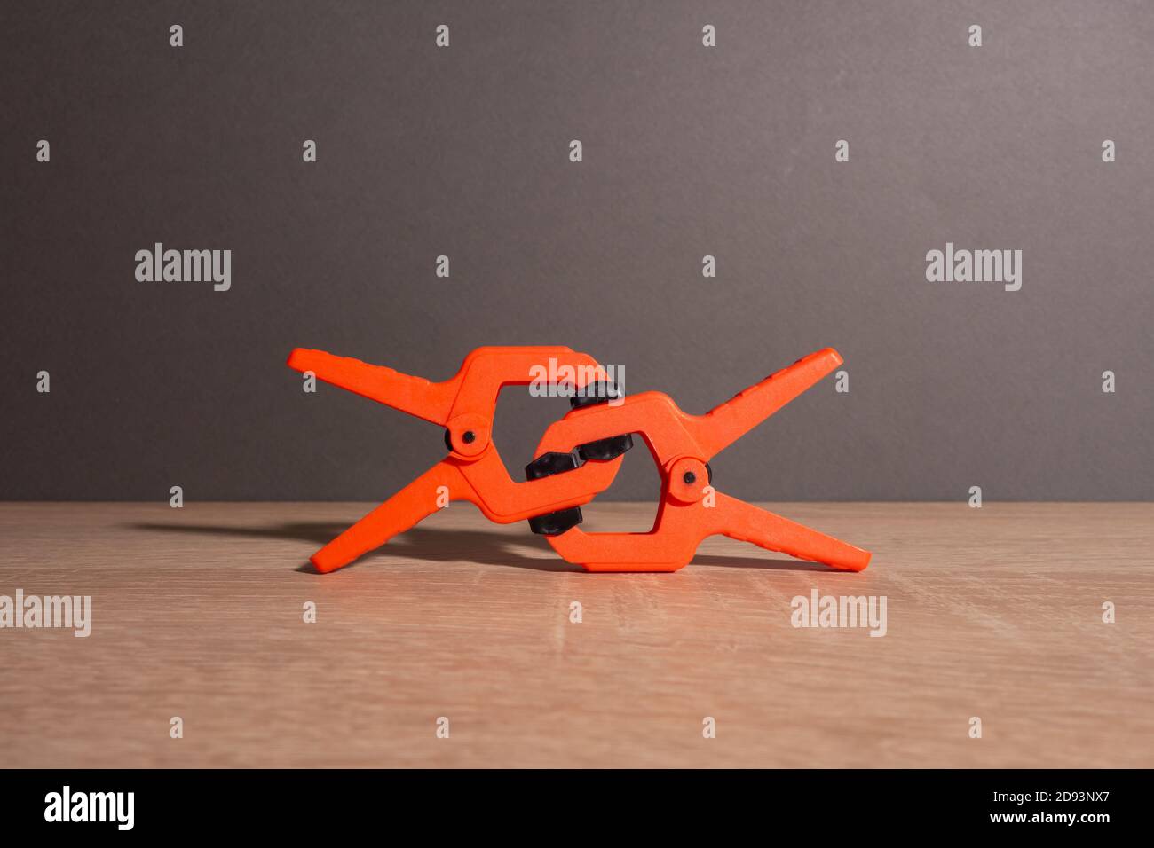 Clothespins, carpentry clamps of orange color lie on a wooden table. A pyramid in the form of a robot made of clamps. Stock Photo