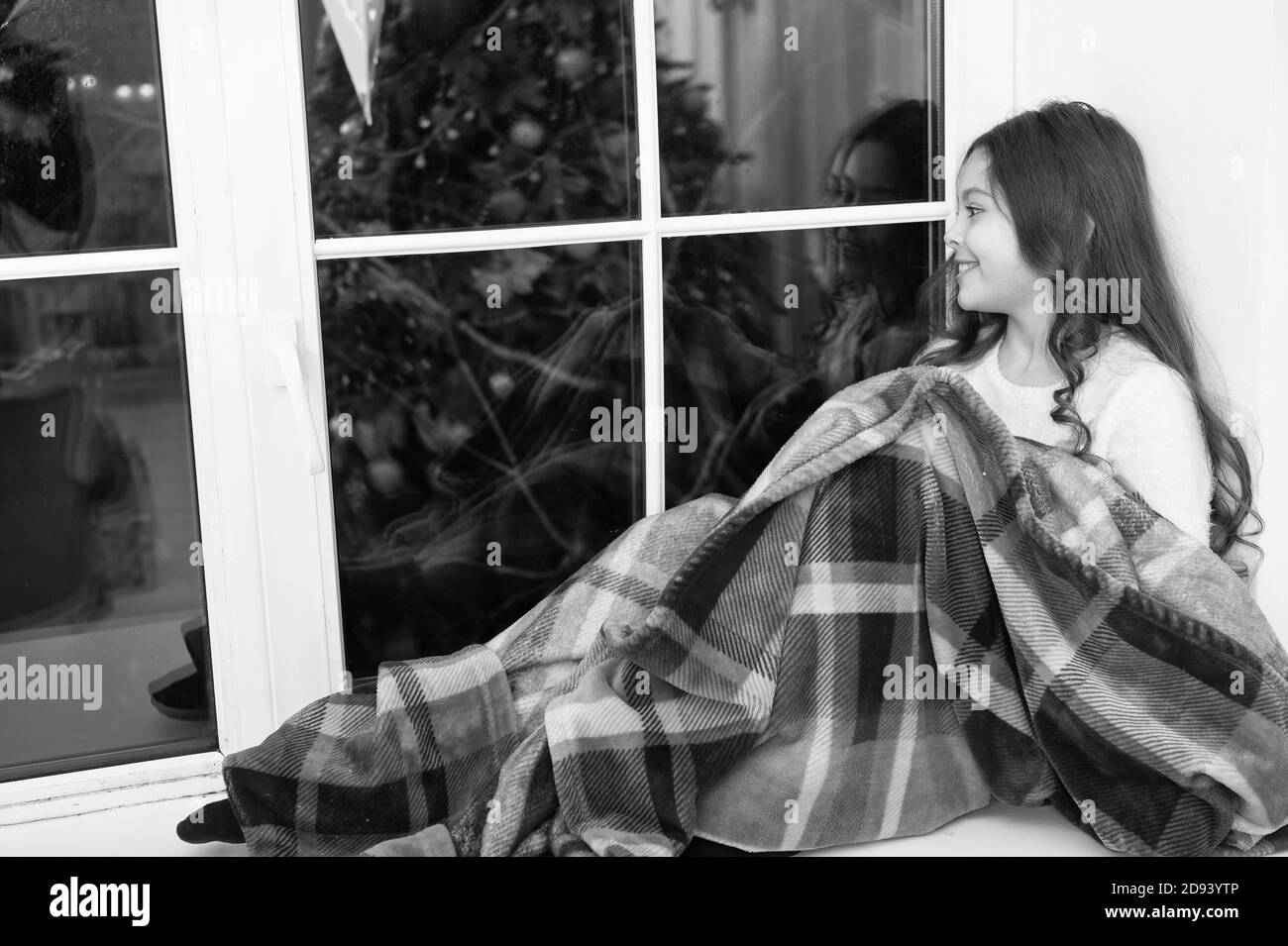 Comfortable and warm. Little child feel comfortable at xmas home. Small girl relax on window sill. Cute kid rest covered in comfortable plaid blanket. Comfortable holiday atmosphere. New year eve. Stock Photo