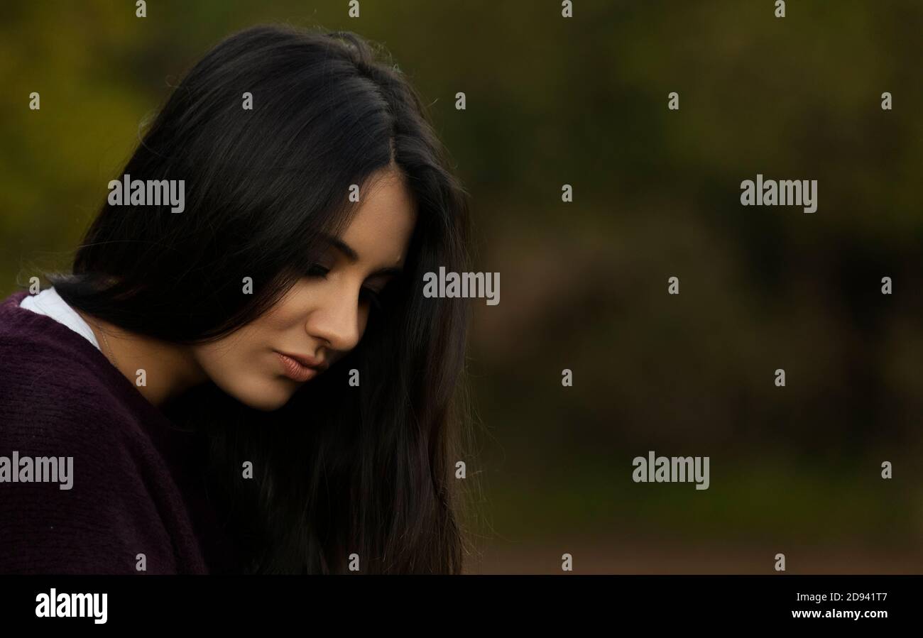 Pretty sad girl looking down in a blur countryside background Stock Photo