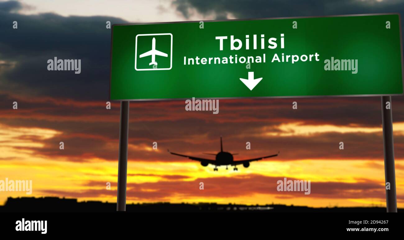 Airplane silhouette landing in Tbilisi, Georgia. City arrival with airport direction signboard and sunset in background. Trip and transportation conce Stock Photo
