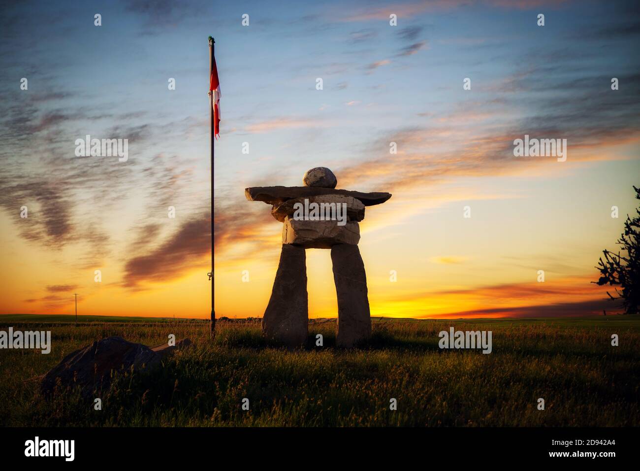 A large Inukshuk rock statue beside the Canadian flag in countryside