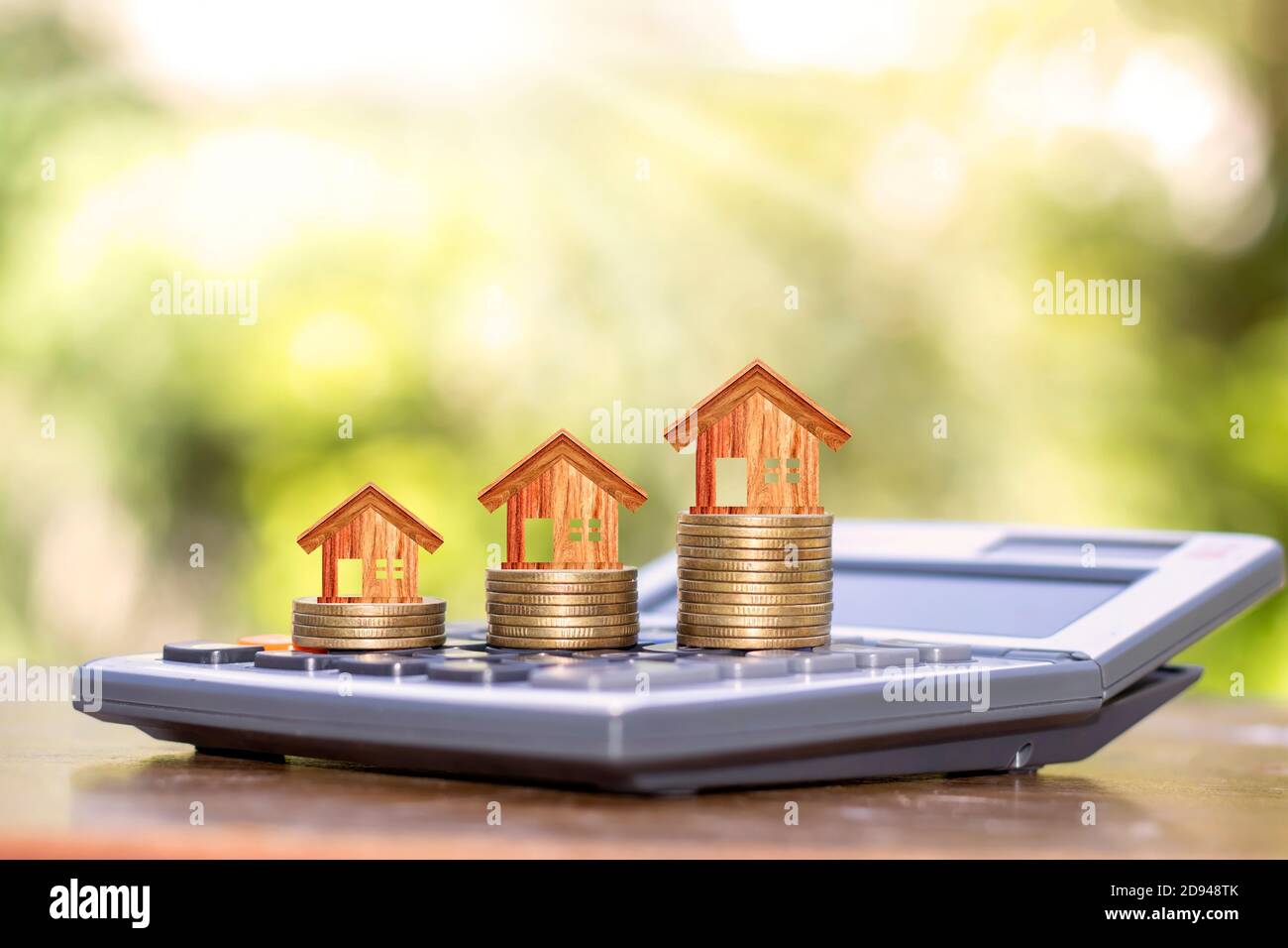 Wooden house designs on coins, including real estate investment ideas calculator. Stock Photo