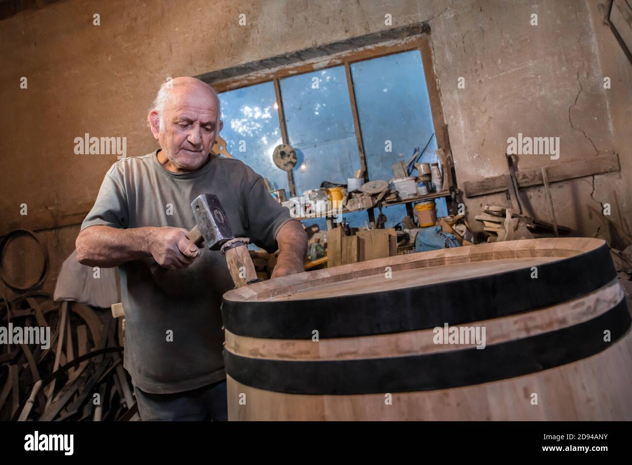 Production of wooden wine barrels. The master makes a wooden jars and barrels for wine.  Oak boards compresses them with iron rings Stock Photo