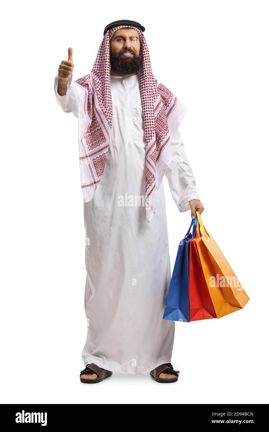 Full length portrait of an arab man in a thobe holding shopping bags and showing thumbs up isolated on white background Stock Photo