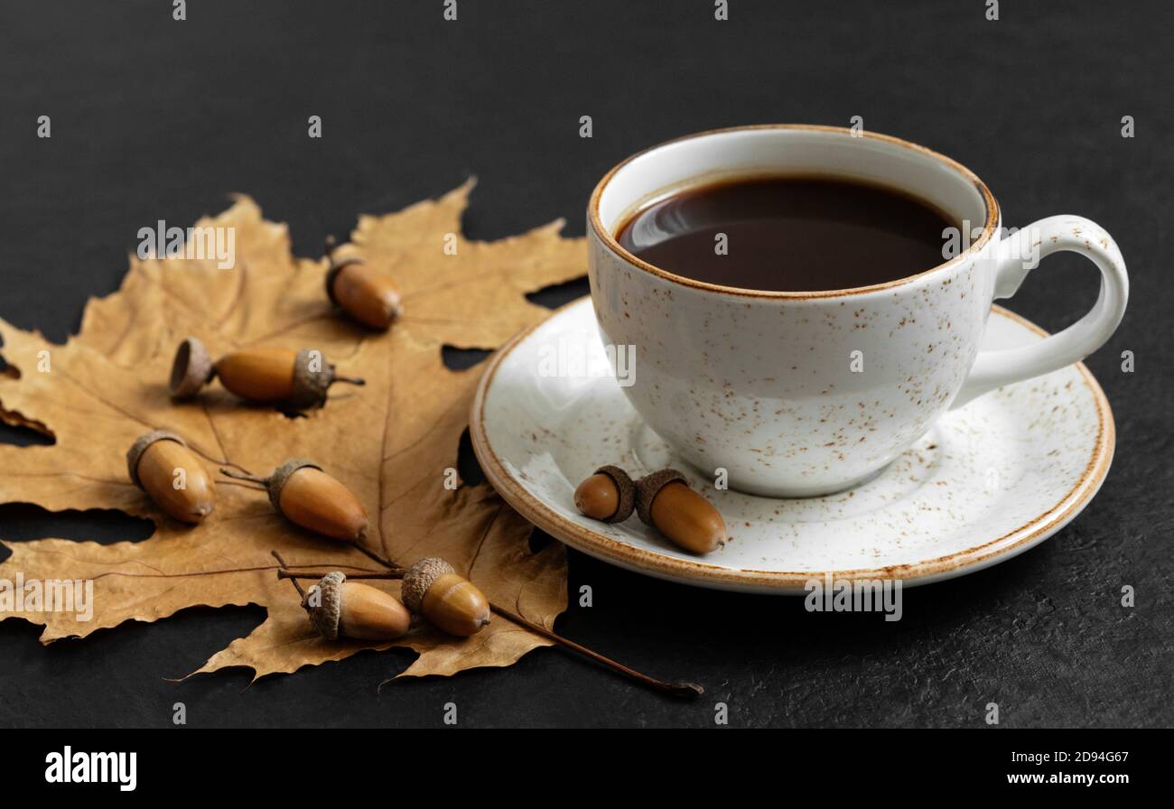 Autumn still life with a cup of coffee, leaves and acorns on a black