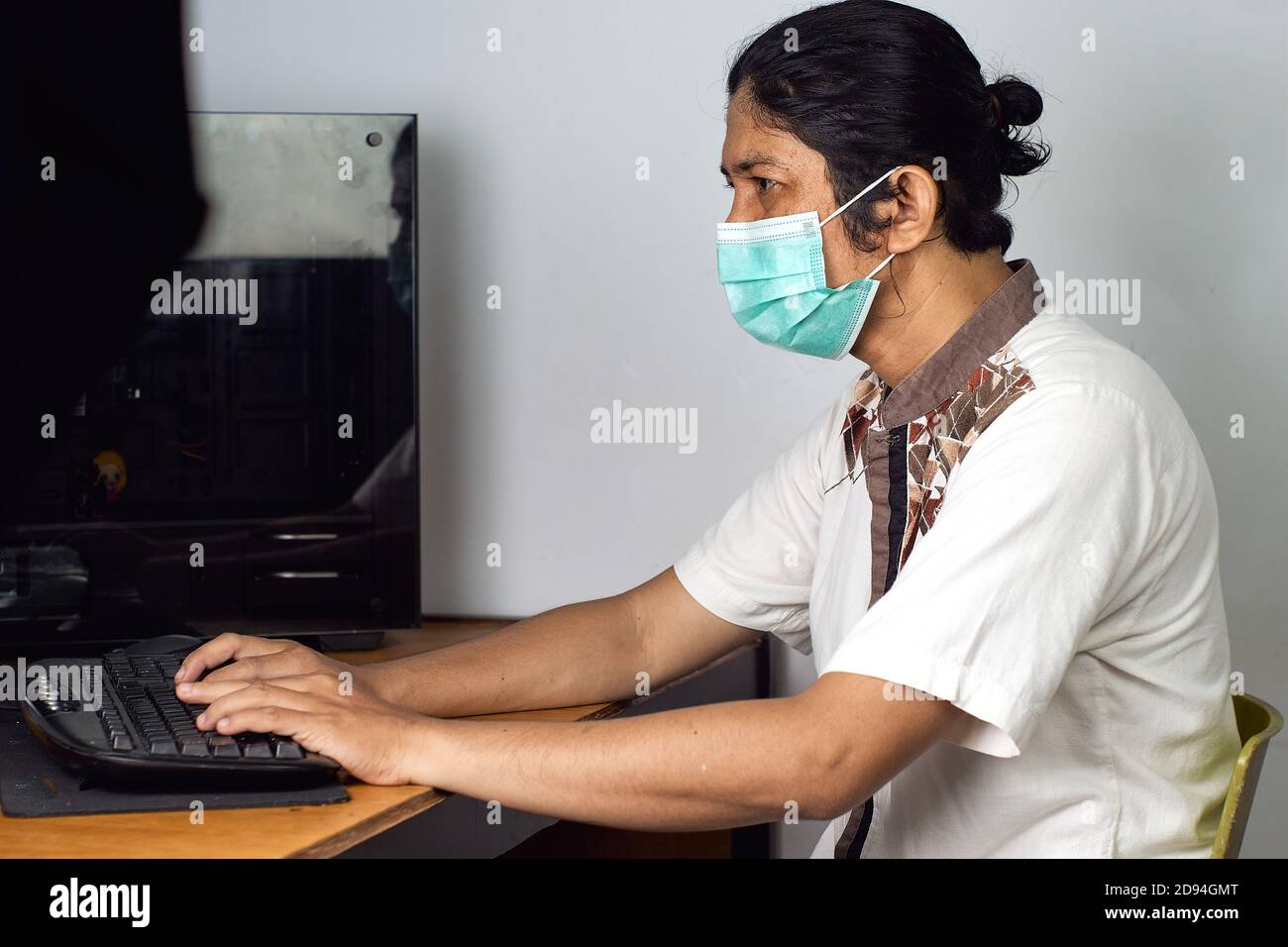 Asian man use surgical mask work on front of computer during pandemic virus situation. People in protective face mask for prevent pandemic virus. heal Stock Photo