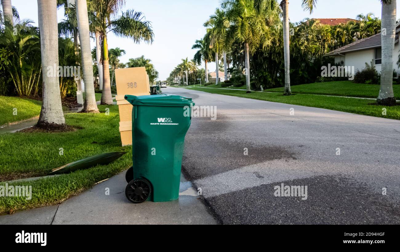 Green and yellow waste management garbage cans at the curb for trash pick up day in a sunny