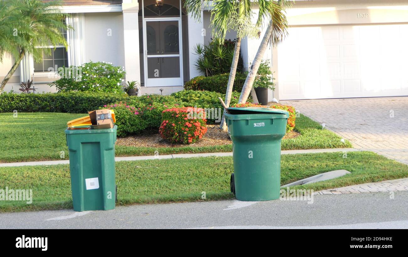 Green and yellow waste management garbage cans at the curb for trash pick up day in a sunny