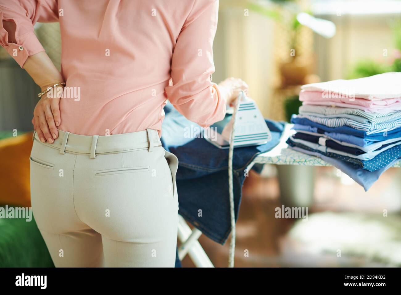Seen From Behind Woman In Pink Shirt And White Pants With Pile Of Folded Ironed Clothes Having Back Pain While Ironing On Ironing Board In The House I Stock Photo Alamy alamy