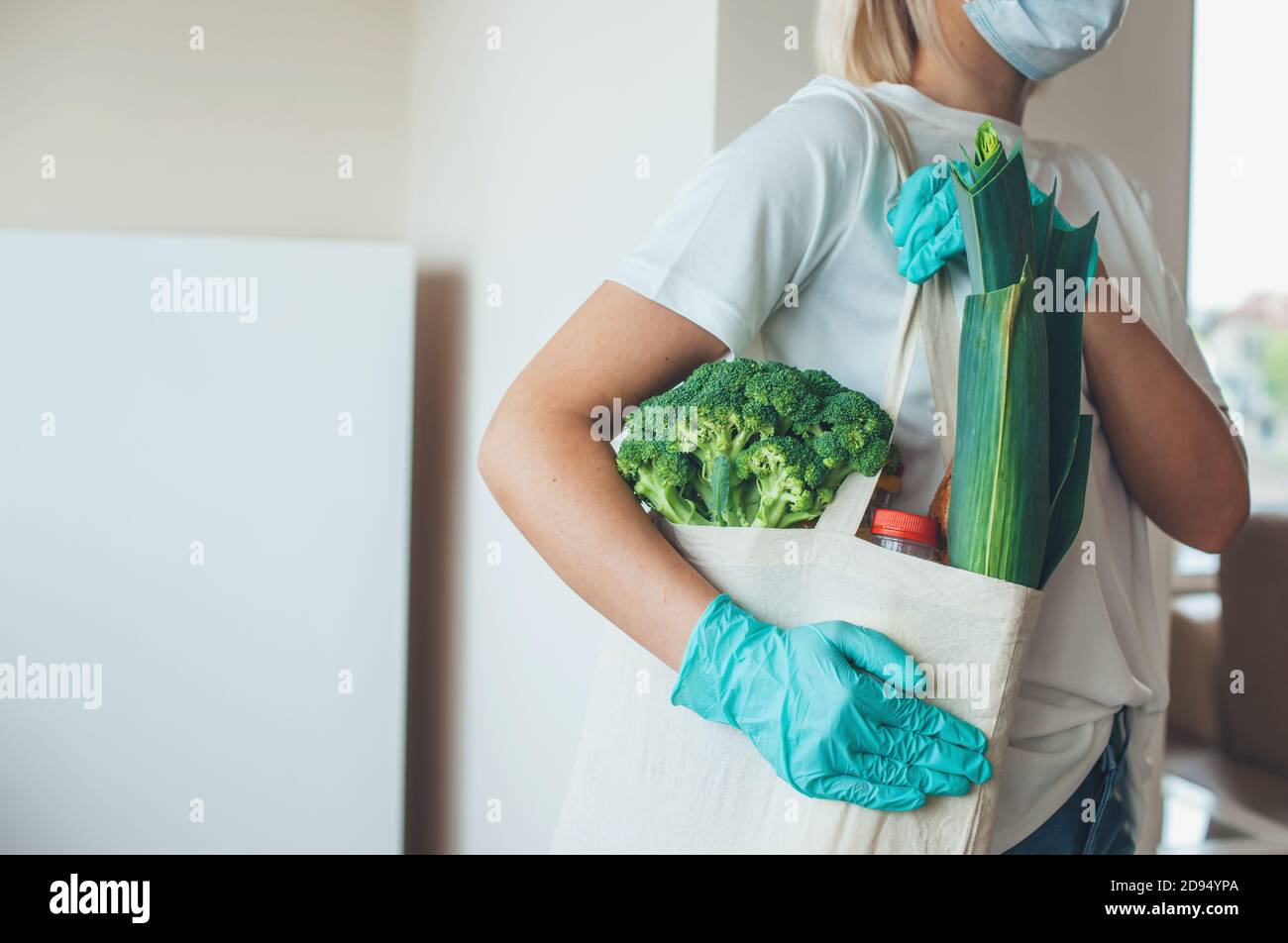 Blonde woman with gloves and mask is delivering food in a bag during ...