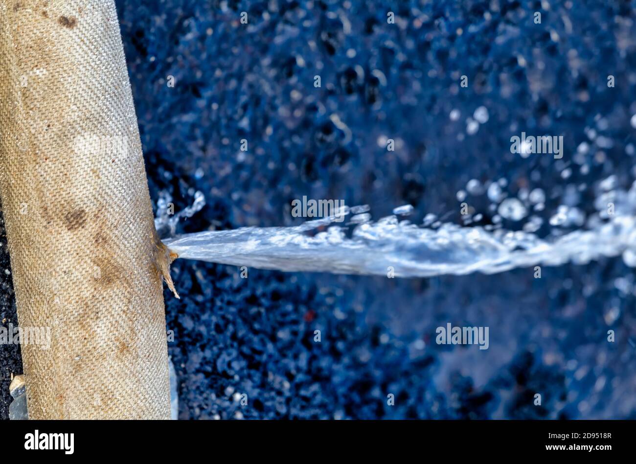 Water leaking from the hole in a hose on asphalt. Old broken leaking hose pipe of industrial