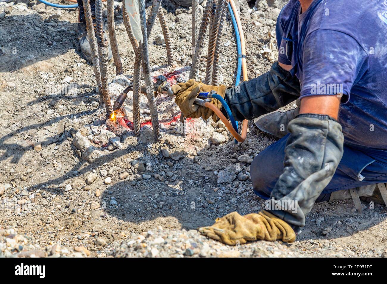Worker cutting concrete reinforcing metal rods with torch at building