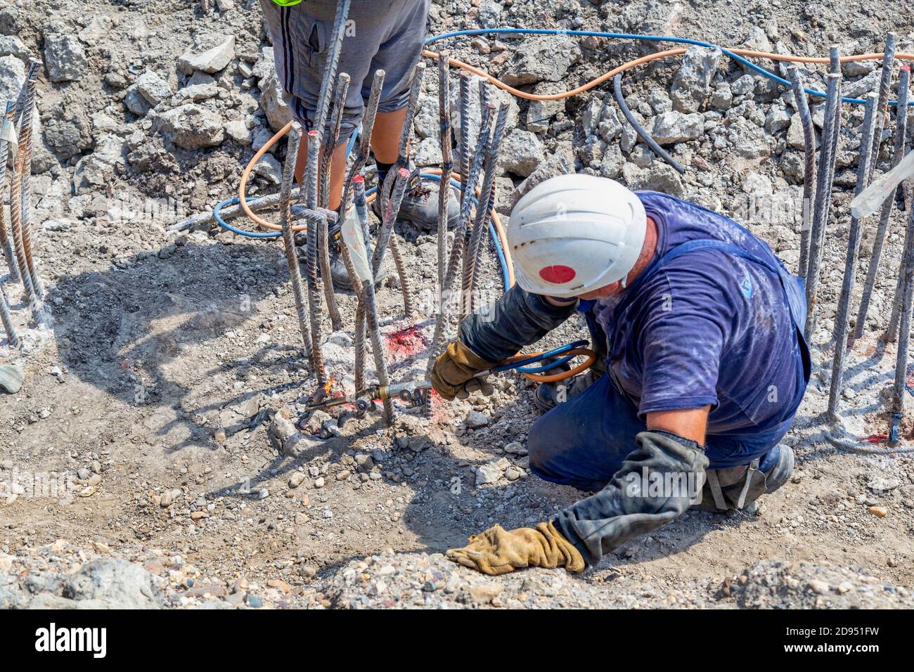 Workers cutting concrete reinforcing steel rods with torch at building ...