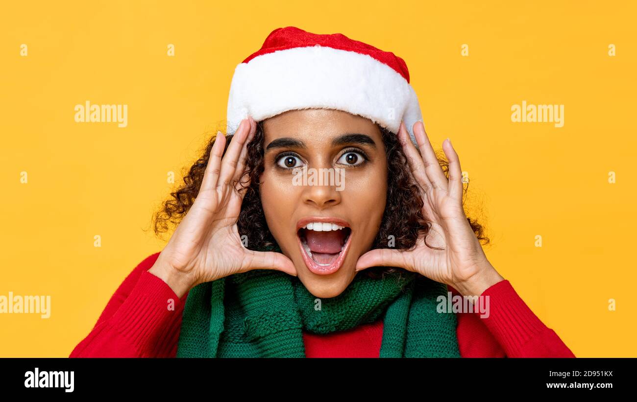 Shocked woman in Christmas attire yelling with hands cupped around face on yellow isolated studio background Stock Photo
