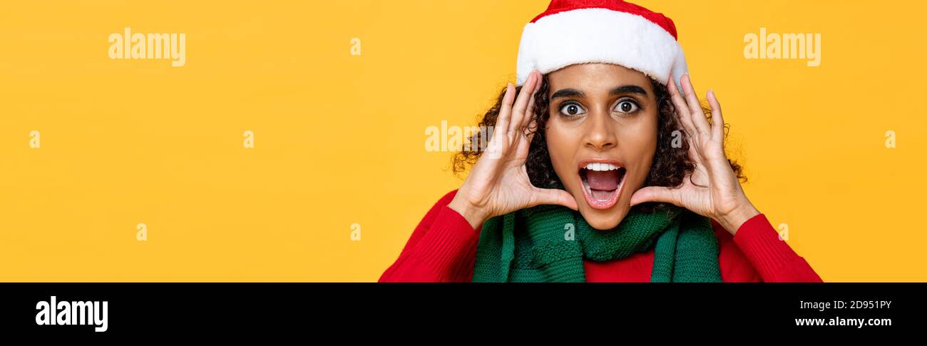 Shocked woman in Christmas attire yelling with hands cupped around face on yellow isolated banner background with copy space Stock Photo