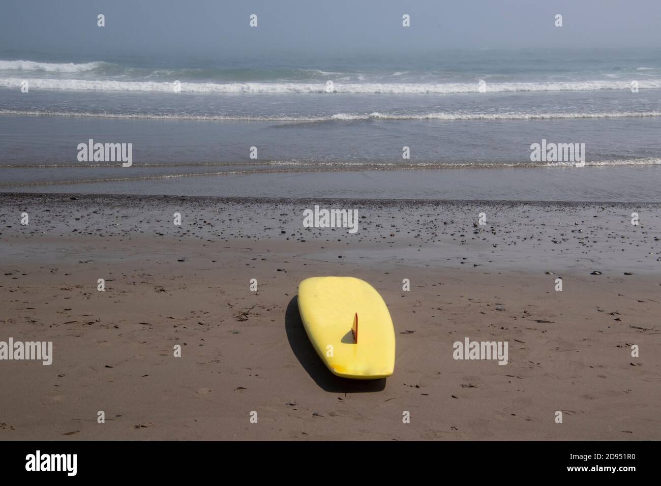 A yellow surfboard sitting on the sand with the waves coming into the ...