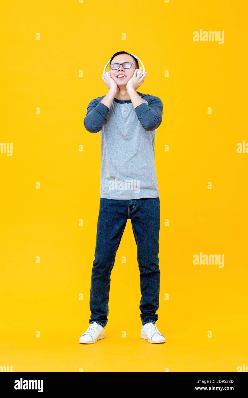 Happy Asian man wearing headphones listening to relaxing music with eyes closed isolated on yellow background Stock Photo
