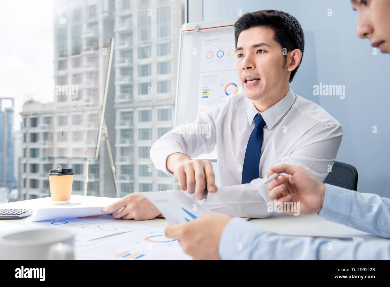 Portrait of Asian businessman analyzing data in an office meeting with colleague in urban setting Stock Photo