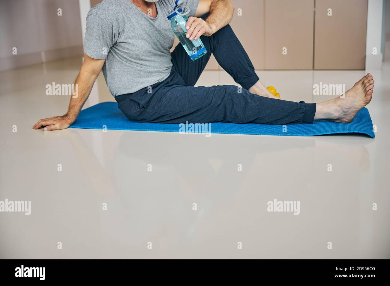 Sporty man with his water bottle sitting on a mat Stock Photo - Alamy