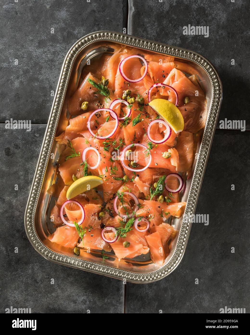 Smoked salmon sliced on tray with lemon, capers and dill. Stock Photo