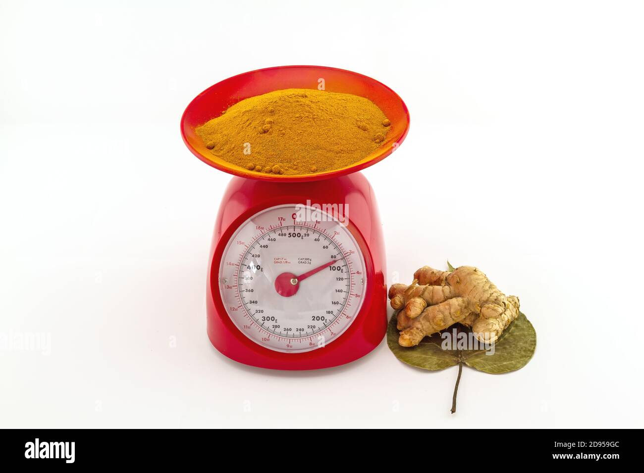 Turmeric powder and fresh turmeric root in red weight scale on white