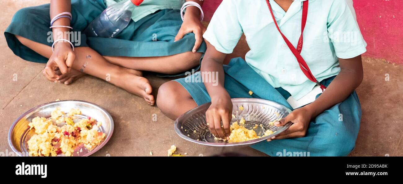 PUDUCHERRY, TAMIL NADU, INDIA - DECEMBER Circa, 2018. Unidentified poor classmates children with uniforms sitting on the floor outdoors, eating with t Stock Photo