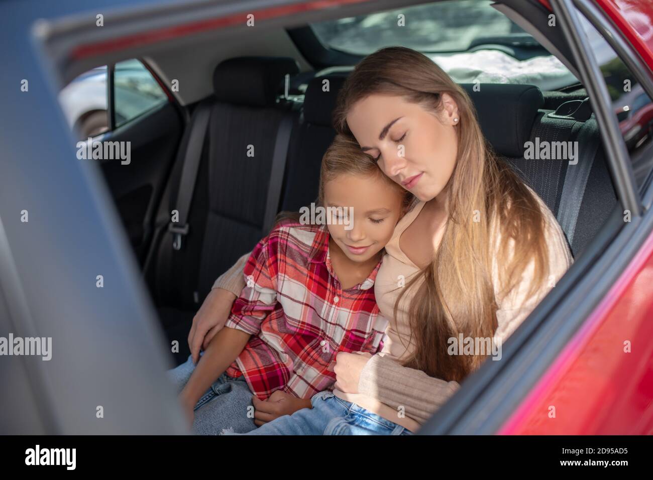 Pleased daughter and her mom hugging, napping on backseat of car Stock Photo