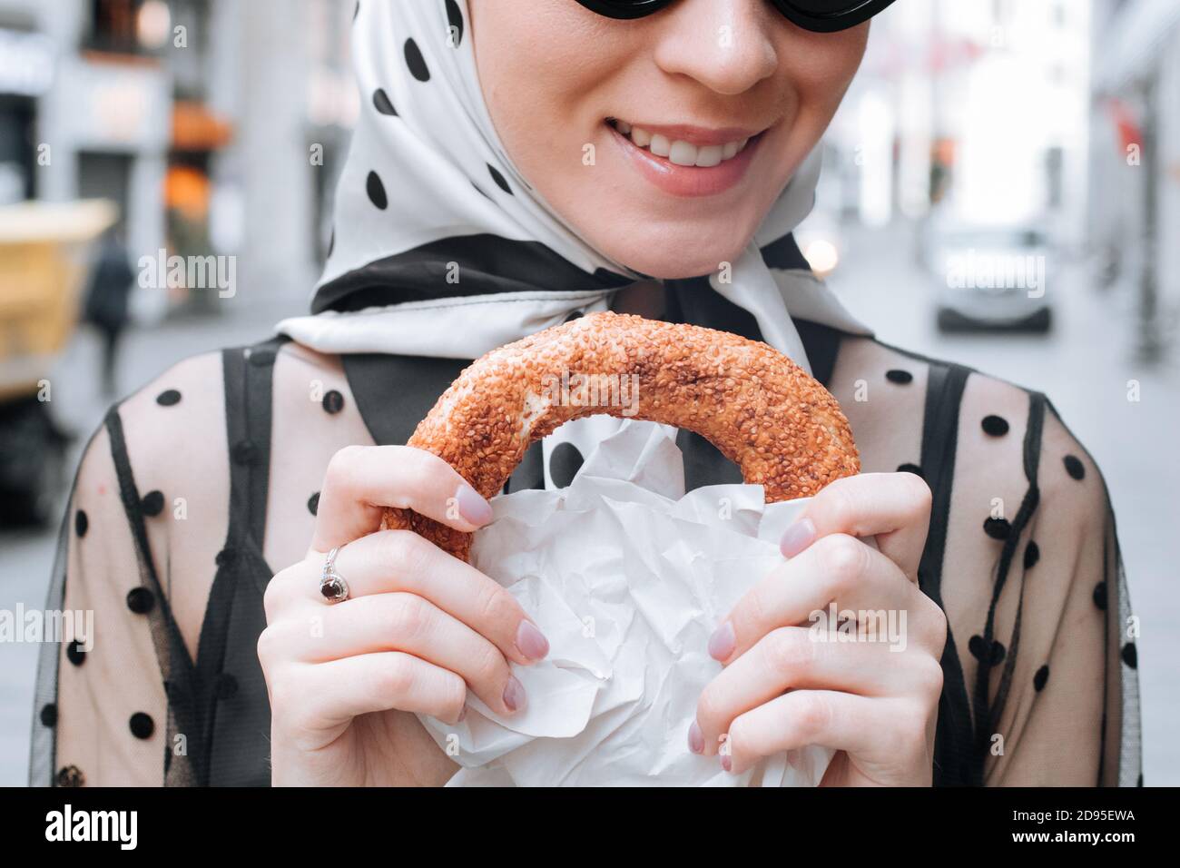 Cute young woman holding in hand traditional Turkish simit in a female hand. Crispy bagel with sesame seeds Stock Photo