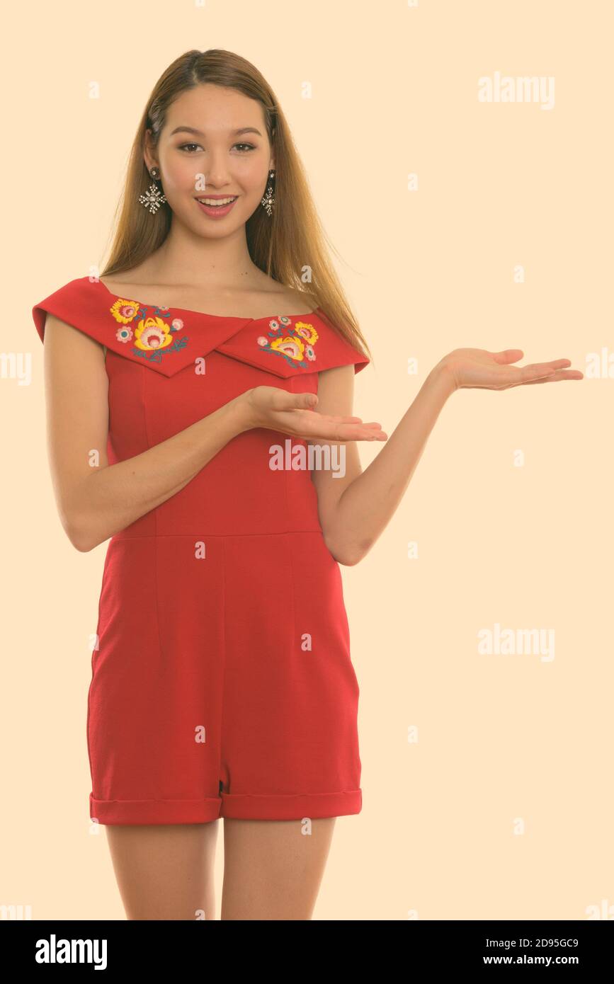 Studio shot of young happy beautiful Asian woman smiling and standing ...
