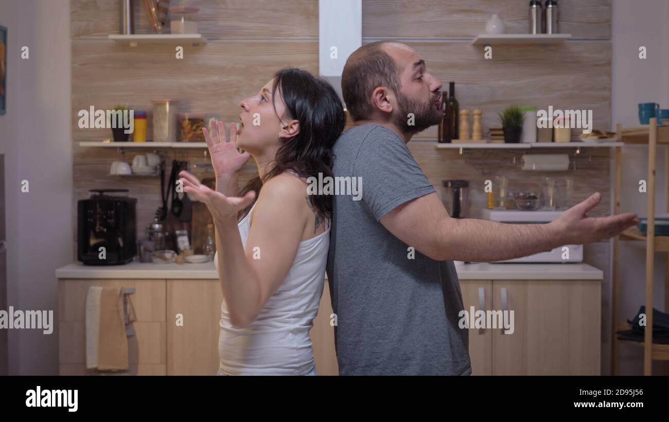 Angry people arguing standing back to back. Furious, irritated, frustrated, jealous unhappy couple screaming accusing to each other having family conflict disputing sitting in the kitchen. Stock Photo