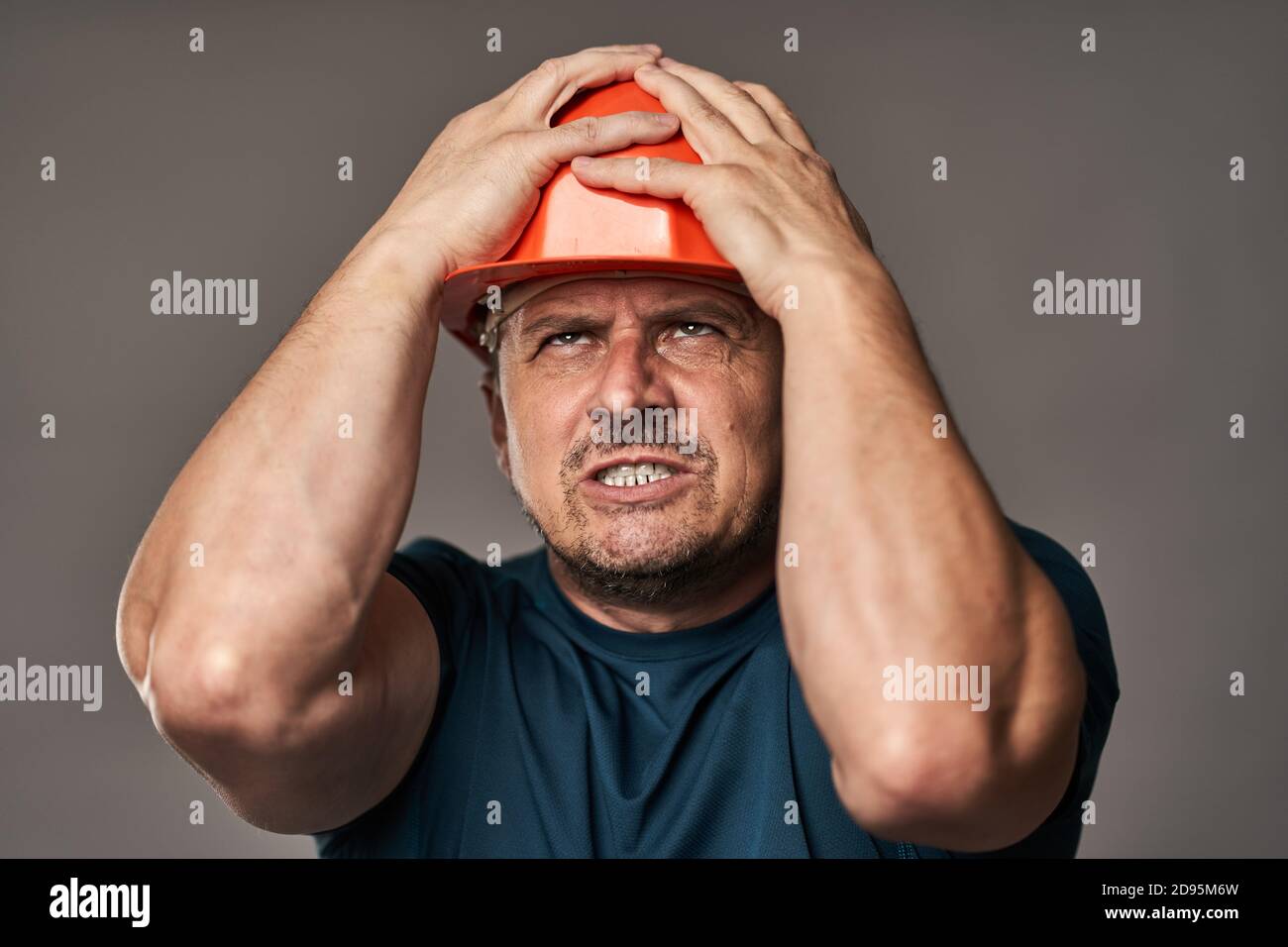 Extremely stressed engineer in hardhat against gray background Stock Photo
