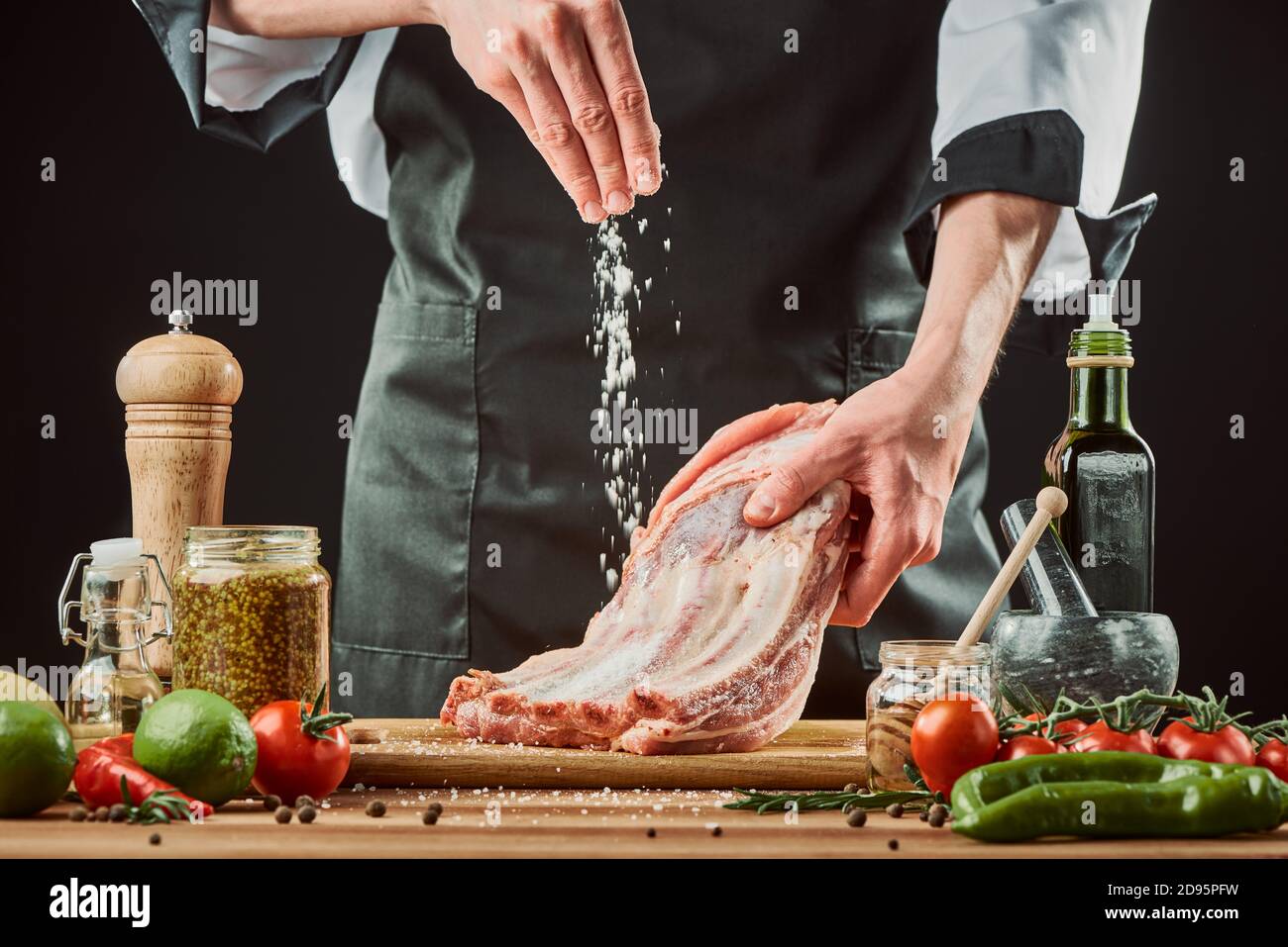 Chef salting raw beef ribs, throwing a big pinch onto the piece of meat