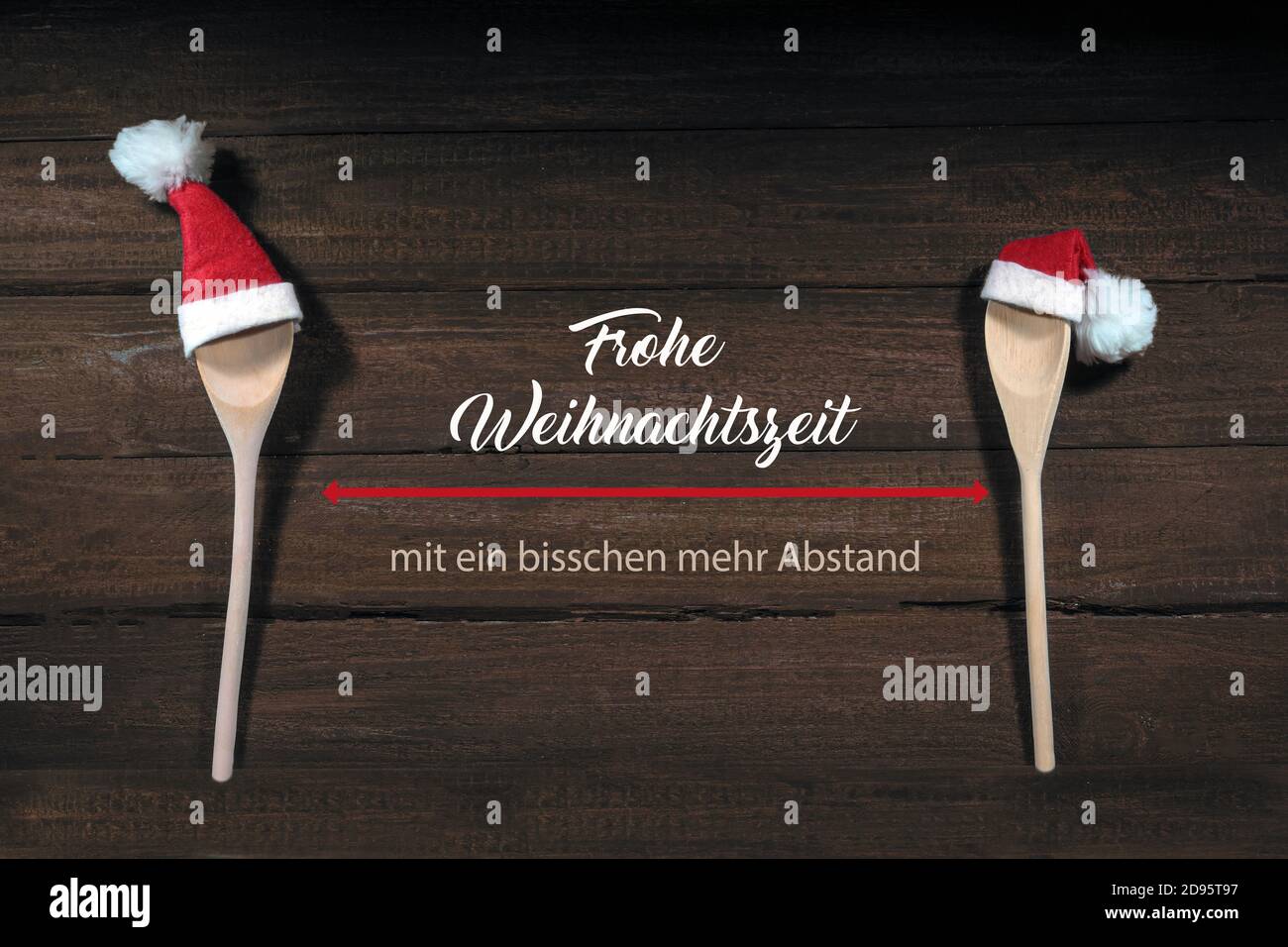 Two cooking spoons with red Santa Claus hats, German text Frohe Weihnachtszeit mit ein bisschen mehr Abstand, meaning Merry Christmas with social dist Stock Photo