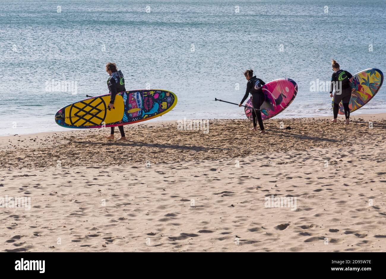Three paddle boarders heading towards the sea with brightly coloured