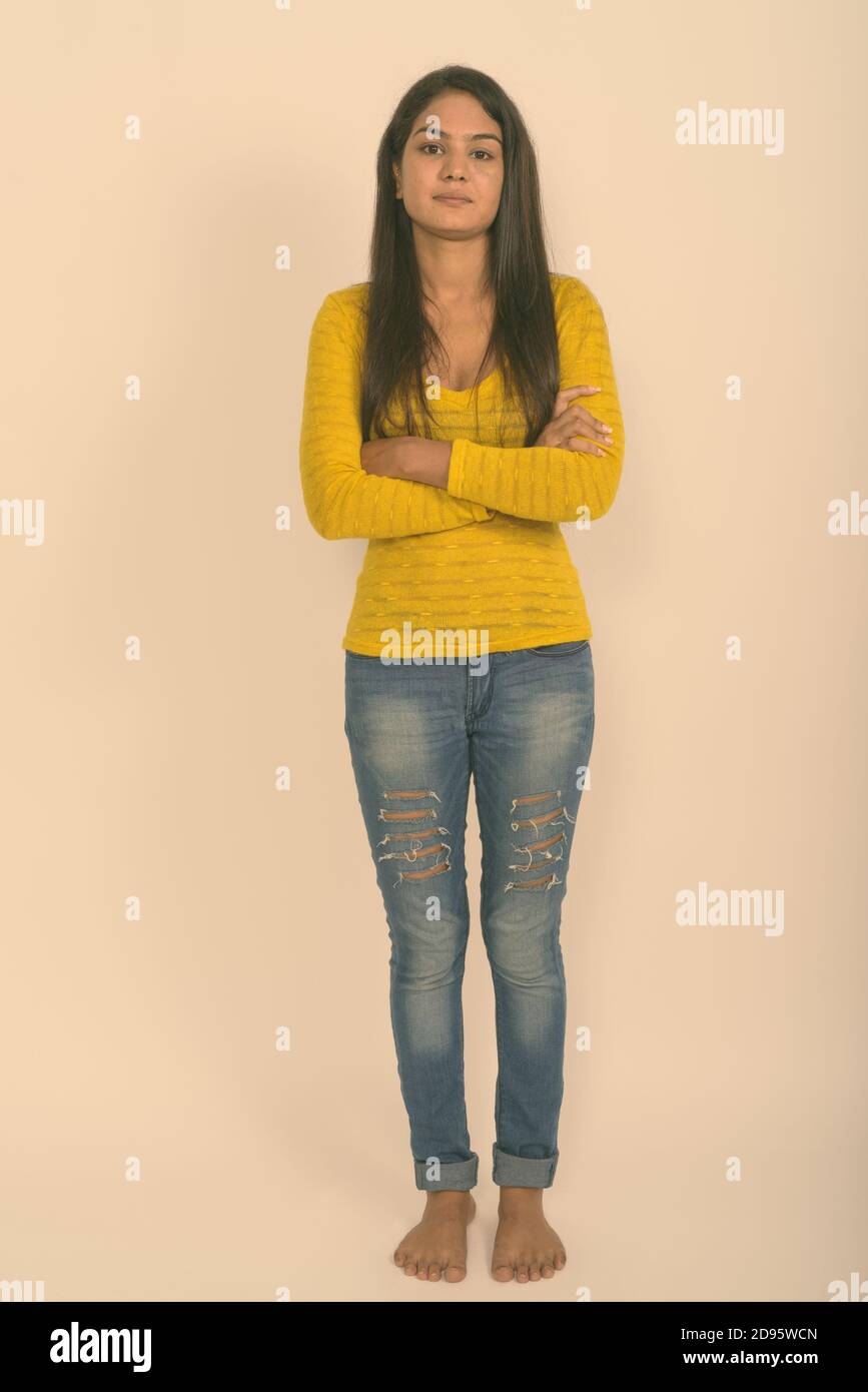 Full body shot of young Indian woman standing with arms crossed barefoot against white background Stock Photo